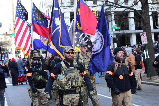 A group of men wearing riot gear holding ameircan flags walking down a street