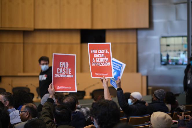 Two people with their hands in the air holding signs that say "end Caste Discrimination" and "End Caste, Racial, and Gender Oppression"