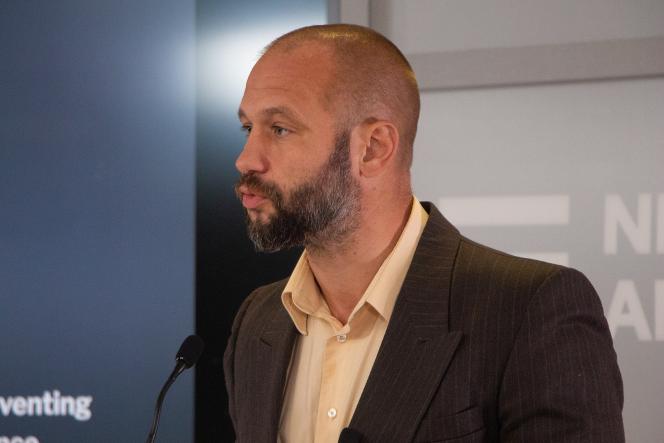 A white bald white man with a salt and pepper beard talking into a mic.