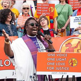 A woman holding a sign that says "one voice, one light, one love, for justice" from Just Texas