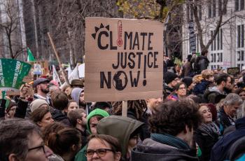 Protesters, and one protesters holding a board that reads "climate justice now!"