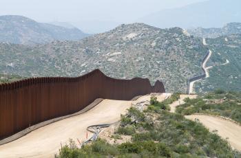 a brown fence following around a dirt road that fades into green mountains.