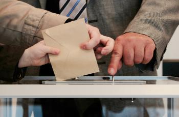 a person dropping an envelope into a ballot box.