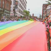 Group of people holding large pride flag above street at pride parade.