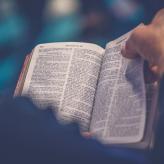 Person's hand turning a page of a Bible.