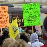 Protesters with signs that say "Obama why are you dividing America? And inciting violence!" and "Obama Why are you collapsing our economy?"