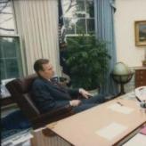 A man in a brown chair leaning back, and a man in leaning forward sitting opposite him.