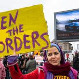 A woman holding a sign that says "open the borders"