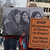 A person holding an image of women crying and a sign that says "stop occupations and torture for empire! The world can't wait!"