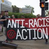 People holding a red and black flag that reads Anti-Racist Action