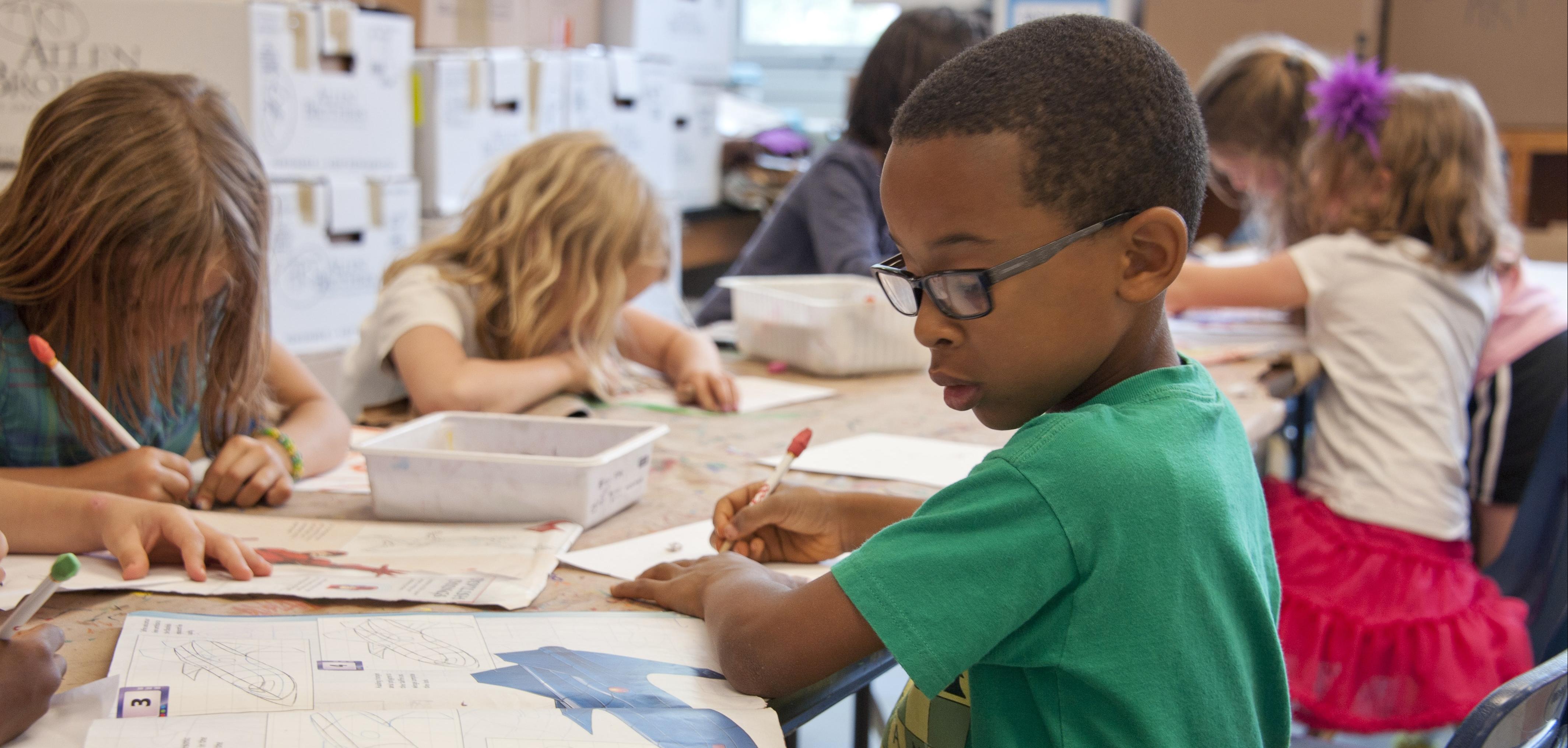 A young boy with glasses in a school, looking at a book.