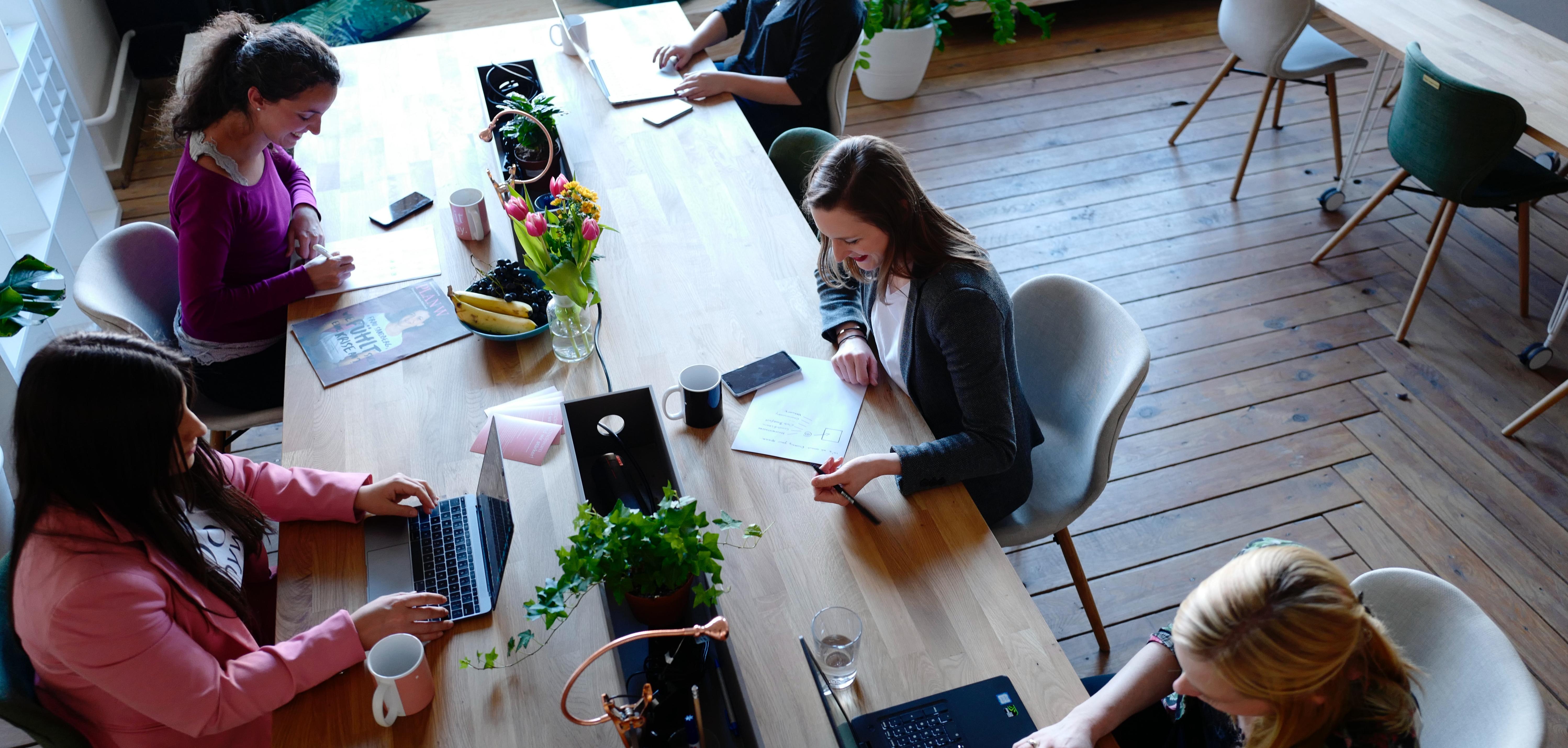 A group of women at a table, with computers and books.