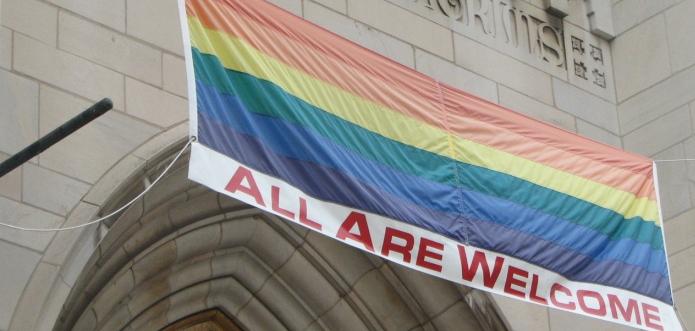 A rainbow flag outside a church with the words "All are welcome"