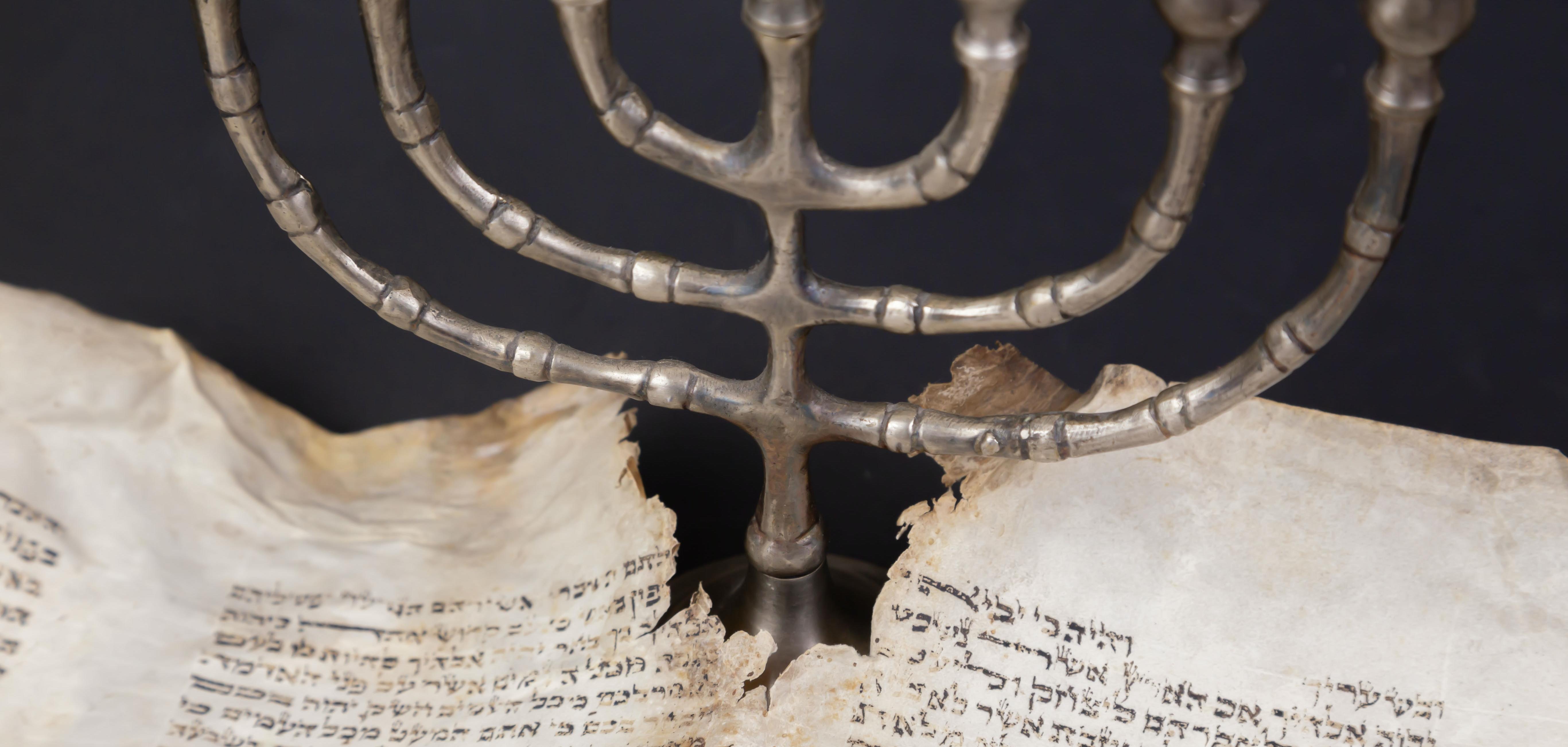 Old scrolls of the Bible and Menorah lie on a black background.