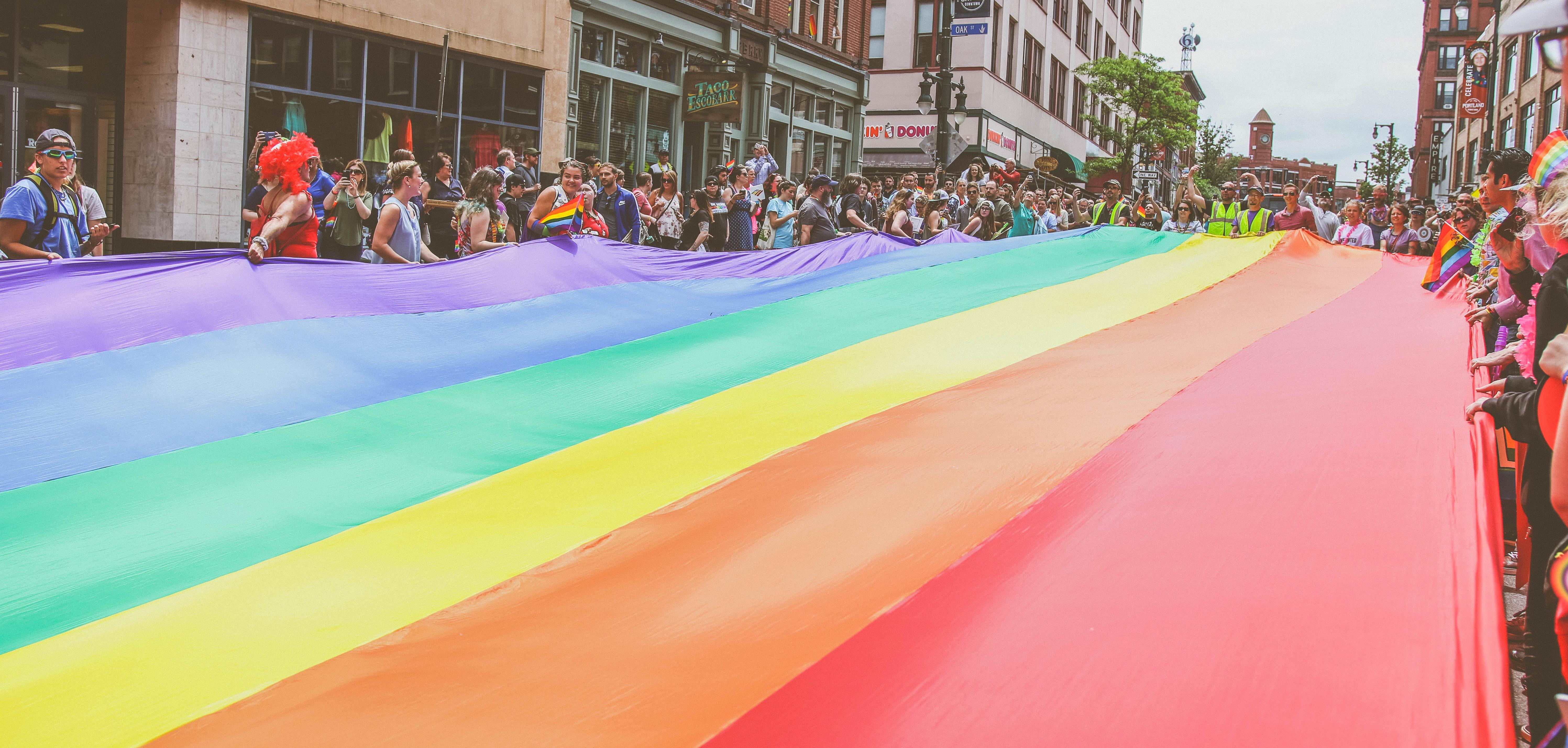 Group of people holding large pride flag above street at pride parade.