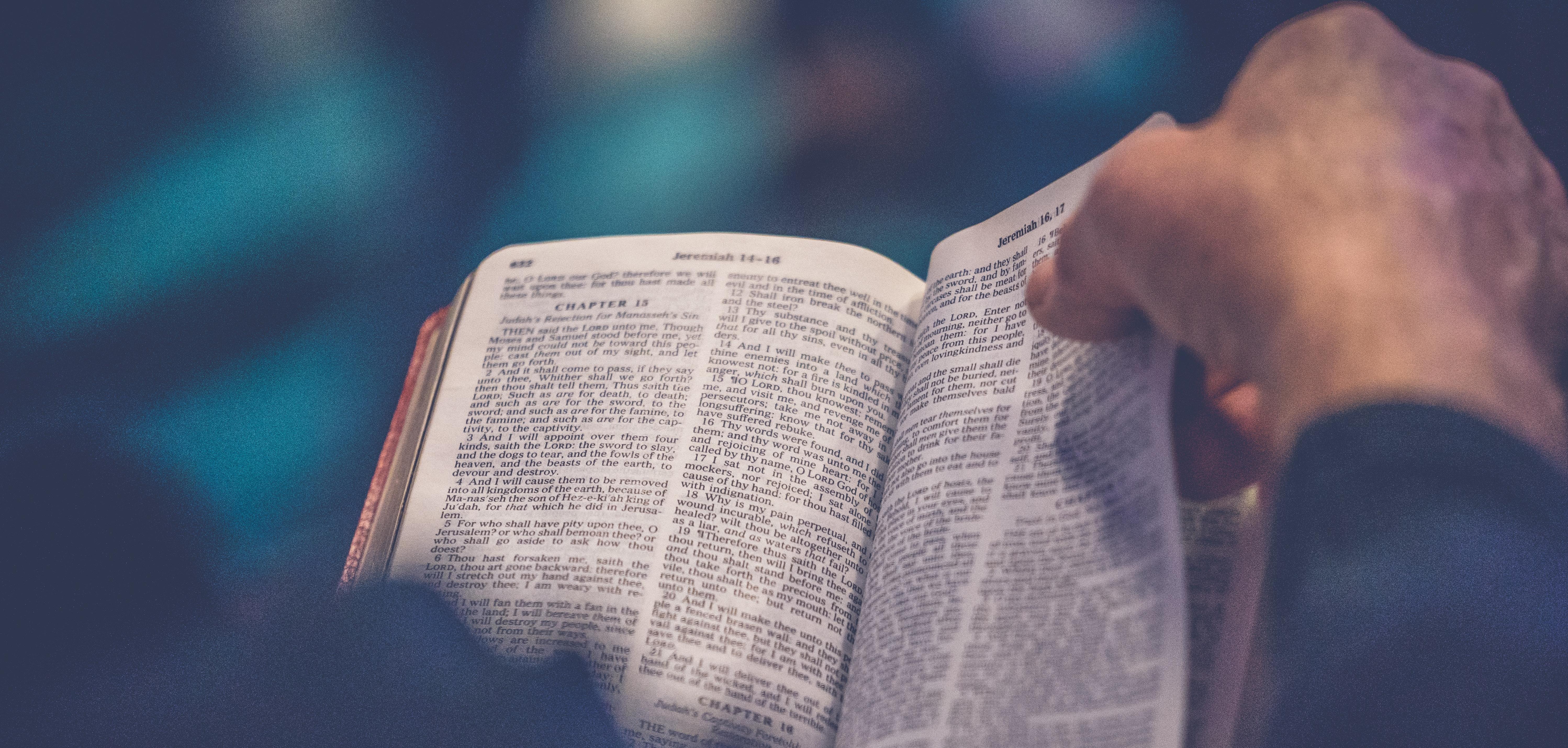 Person's hand turning a page of a Bible.