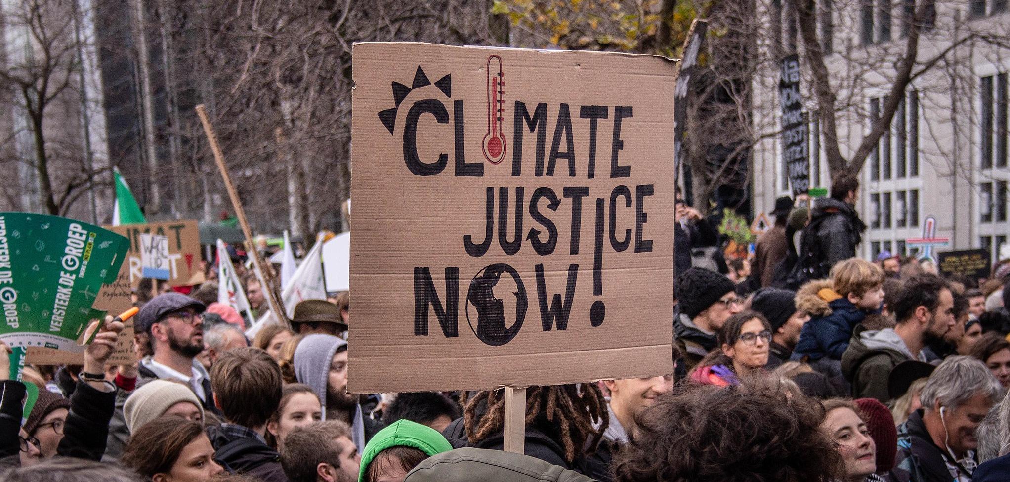 Protesters, and one protesters holding a board that reads "climate justice now!"