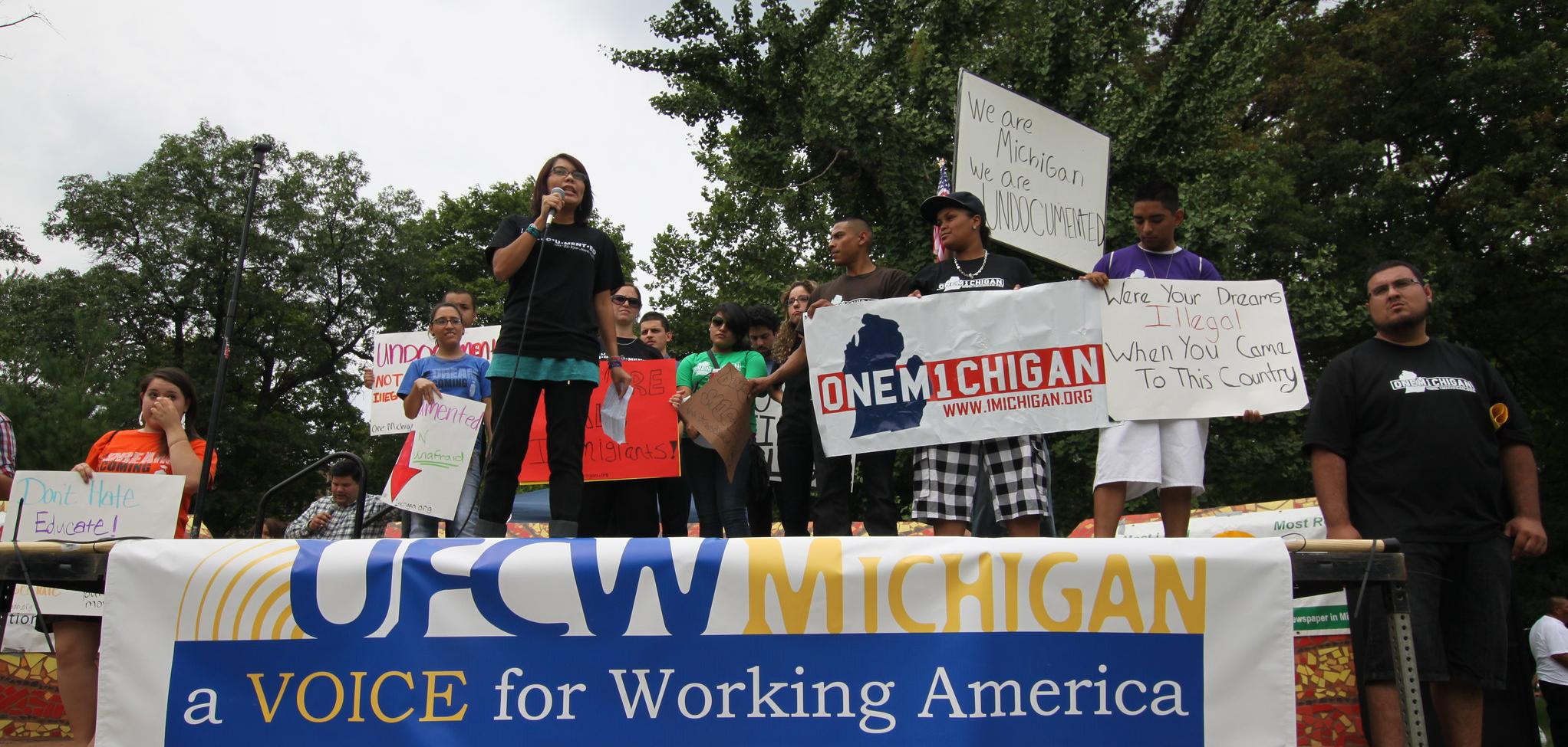 People standing on a platform with a table in front of them with a banner hanging off the table that says "A voice for Working America."