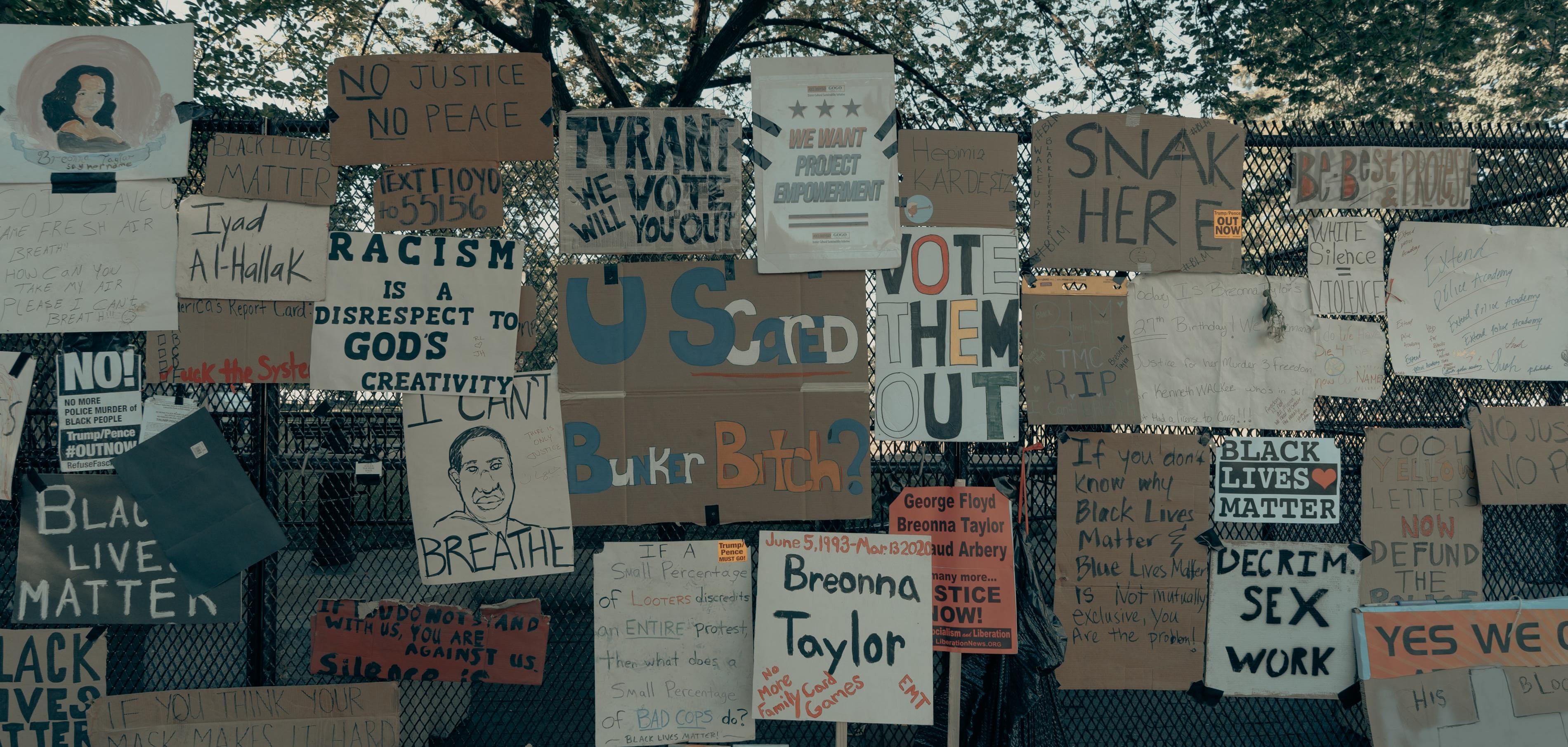 A collection of signs reading slogans for the Black Lives Matter movement covering a fence. 