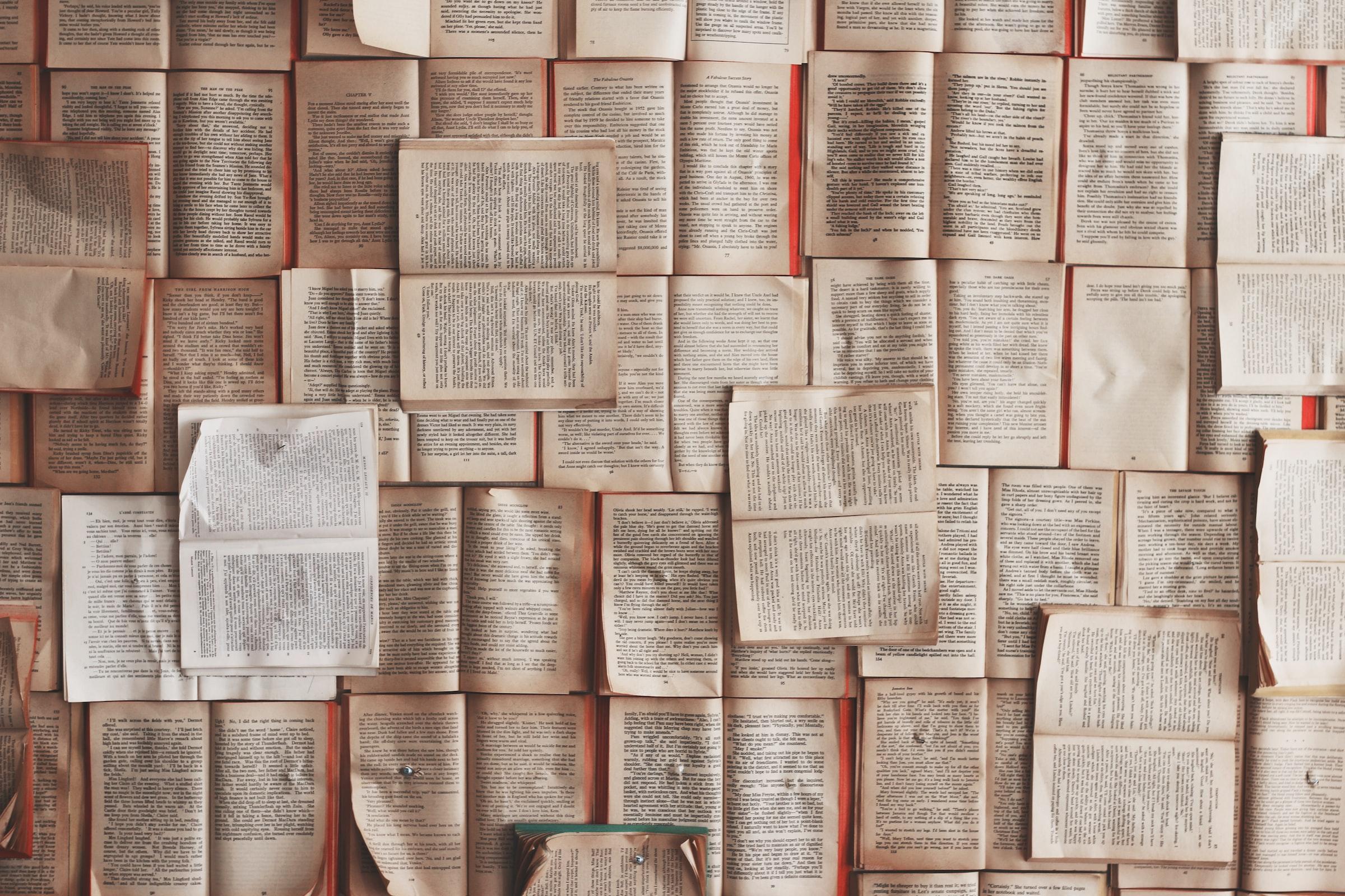 Open books laid horizontally across a table with a couple laid vertically over. 