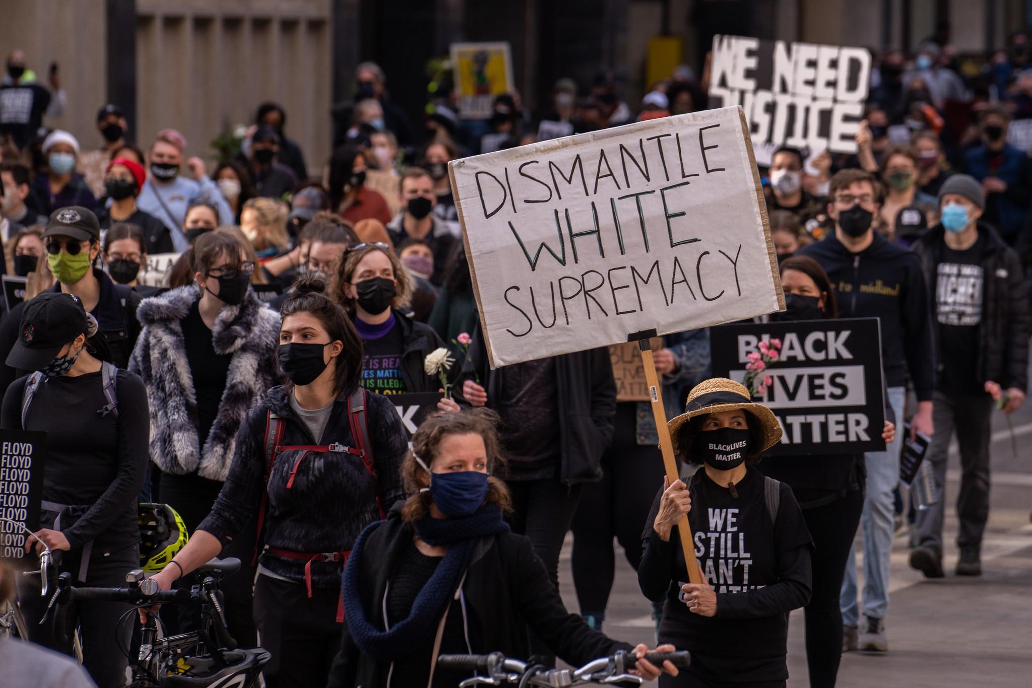 Protestors walking the street, one protestor holding a sign that says "Dismantle White Supremacy."