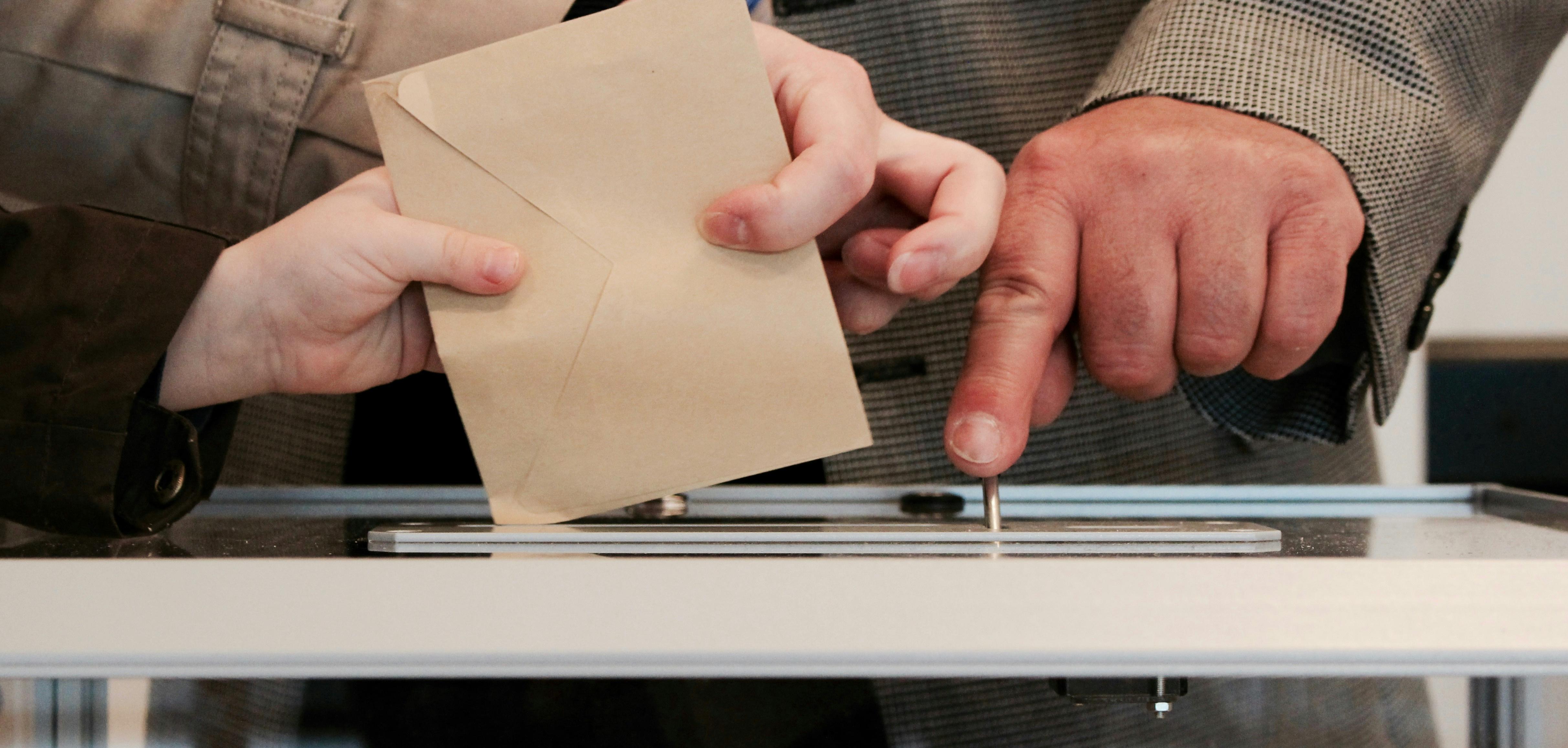 a person dropping an envelope into a ballot box.