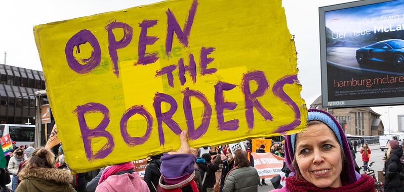 A woman holding a sign that says "open the borders"