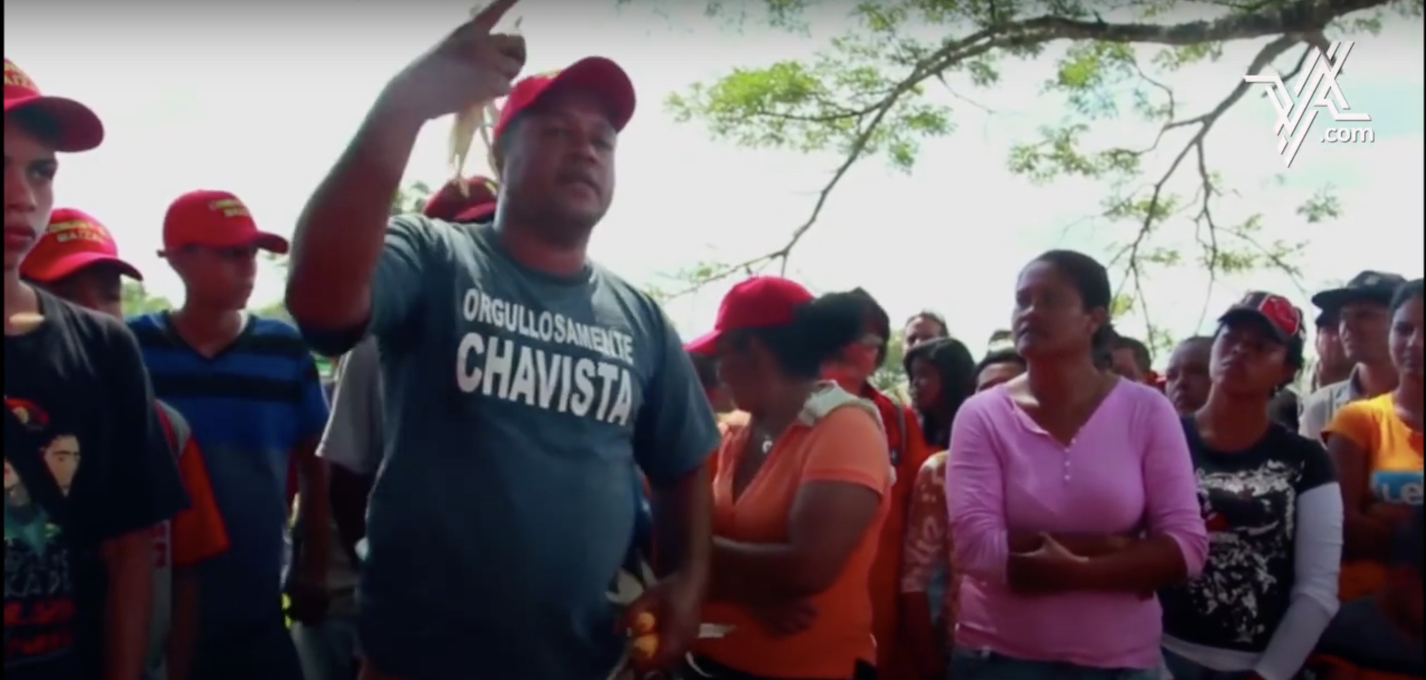 A group of people wearing red hats led by a man speaking with his hand raised. 