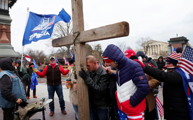 People in winter clothes bowing to a wooden cross.