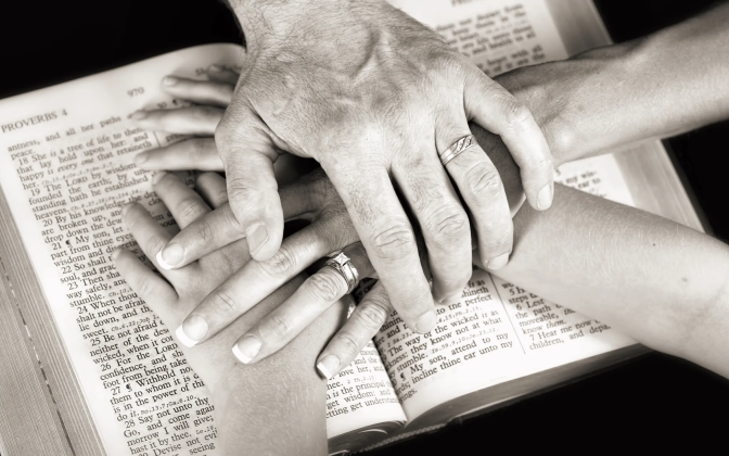 People putting their hands over each other over a book